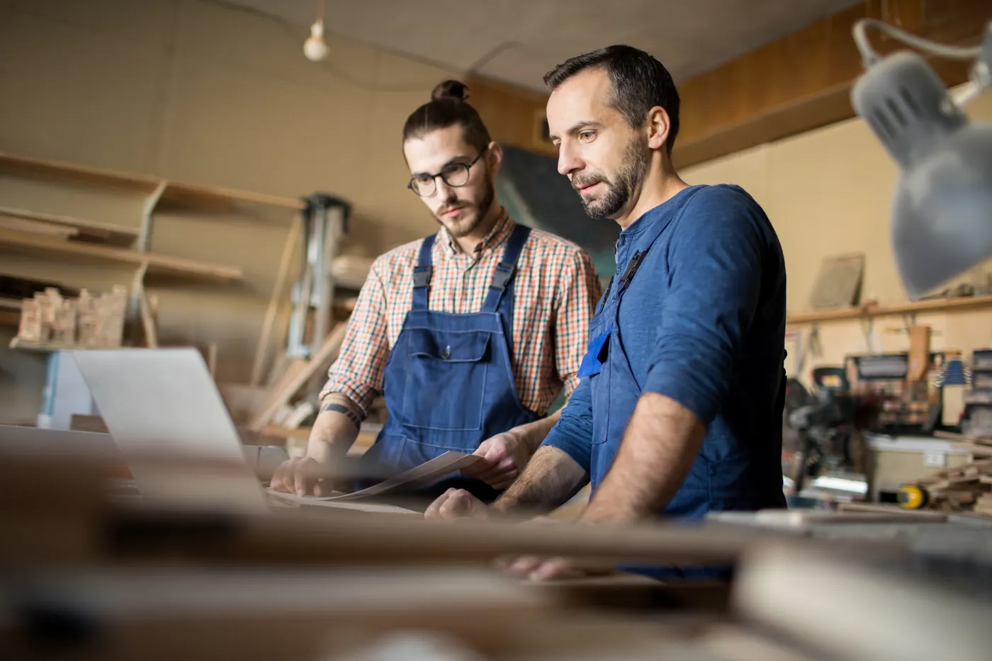 Zwei Handwerker besprechen Unterlagen am Laptop in einer Werkstatt